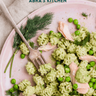 an image of pesto salmon pasta on a pink plate with a fork