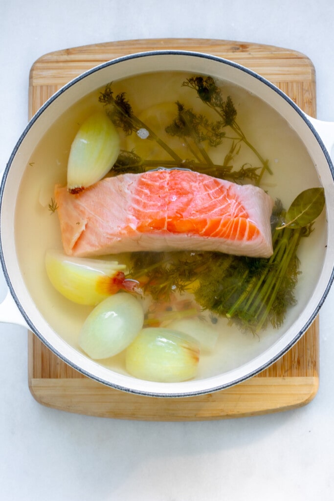 a pot of poaching liquid with a large piece of salmon floating in the liquid