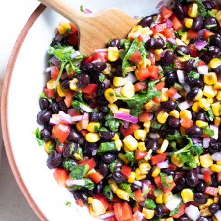 Healthy Corn and Black Bean Salad in a white bowl with a wooden spoon on a white background