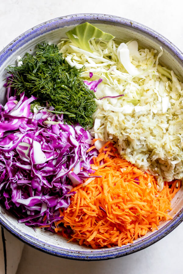 shredded red cabbage, green cabbage, and carrots in a bowl with fresh dill