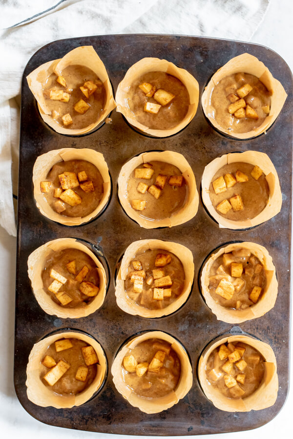 Muffin tray with apple muffin batter and scattered apples on top