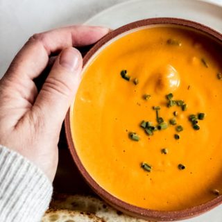 close up shot of hand holding bowl of vegan tomato soup
