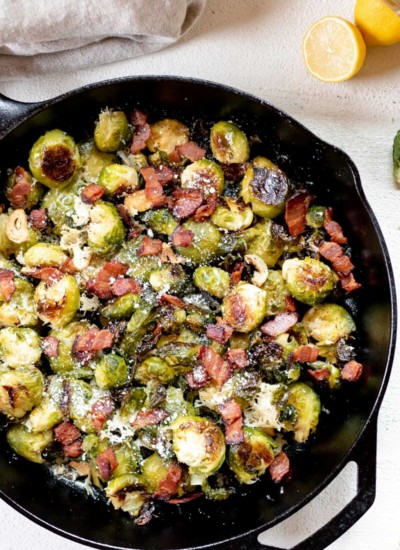 large cast iron pan on white background with Oven Roasted Smashed Brussels Sprouts with Bacon and Parmesan