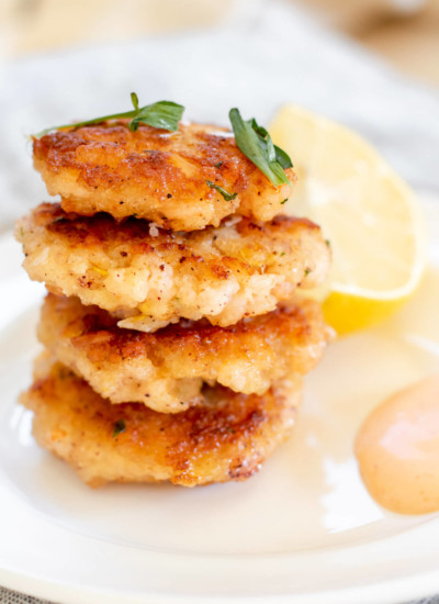 white plate with 4 crispy shrimp cakes stacked high and a lemon on the side