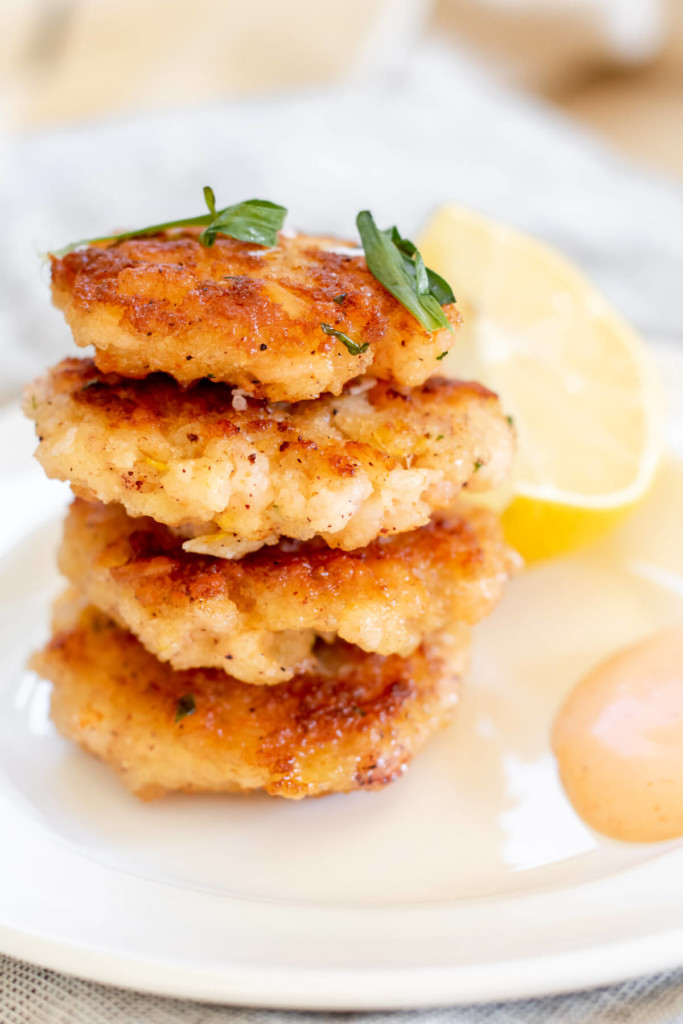 white plate with 4 crispy shrimp cakes stacked high and a lemon on the side