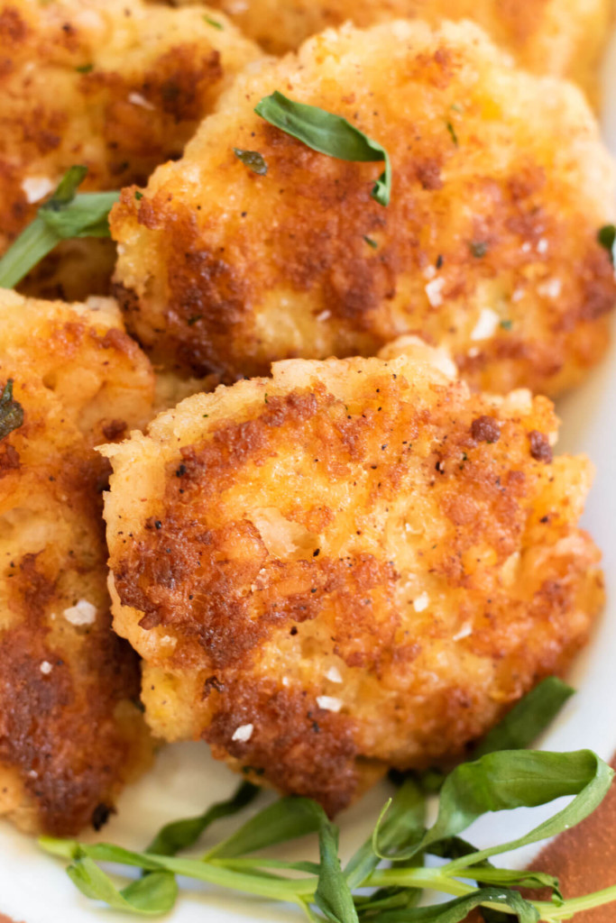 close up shot of a plate of crispy shrimp cakes sprinkled with sea salt and garnished with tarragon