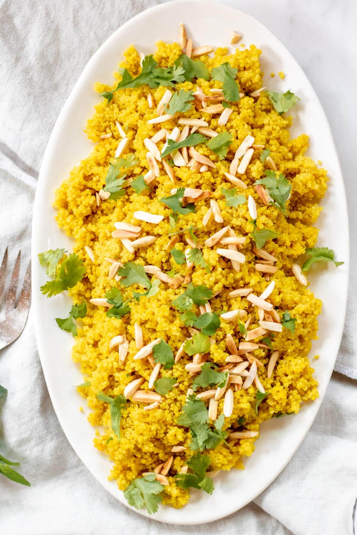 tumeric almond quinoa on a white platter on a grey surface
