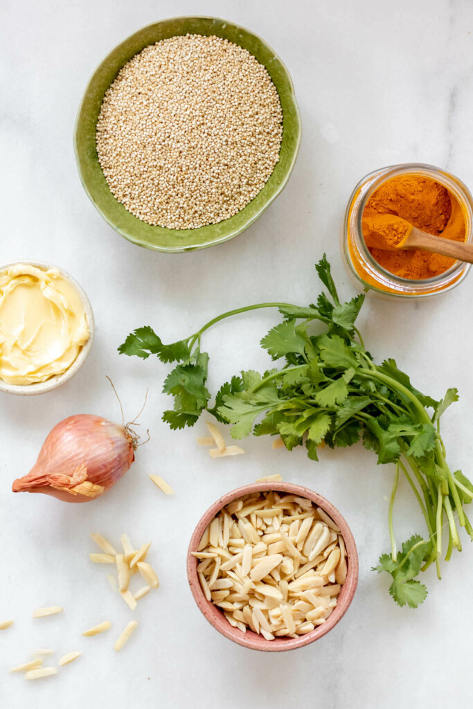 ingredients in small bowls on a white surface, quinoa, turmeric, butter, shallot, almonds, cilantro