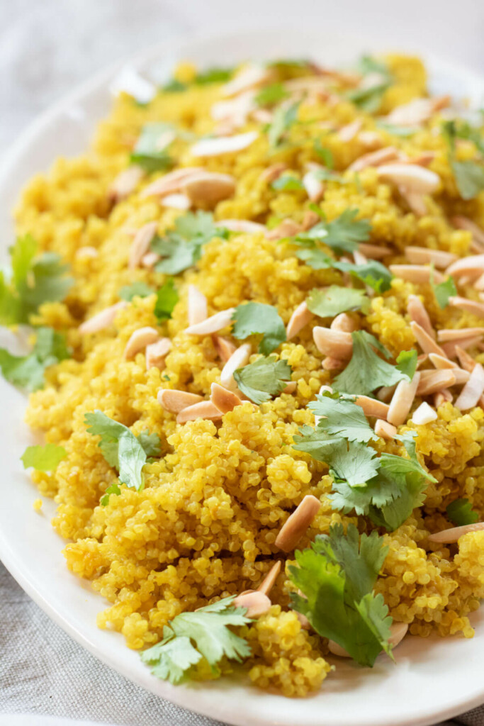 large white platter of bright yellow quinoa with toasted almonds on top and fresh cilantro