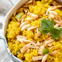close up of blue bowl filled with bright yellow turmeric quinoa with toasted almonds on top and fresh cilantro