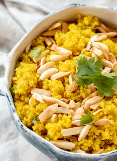 close up of blue bowl filled with bright yellow turmeric quinoa with toasted almonds on top and fresh cilantro