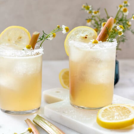 2 glasses filled with rhubarb chamomile margarita and garnished with lemon and rhubarb