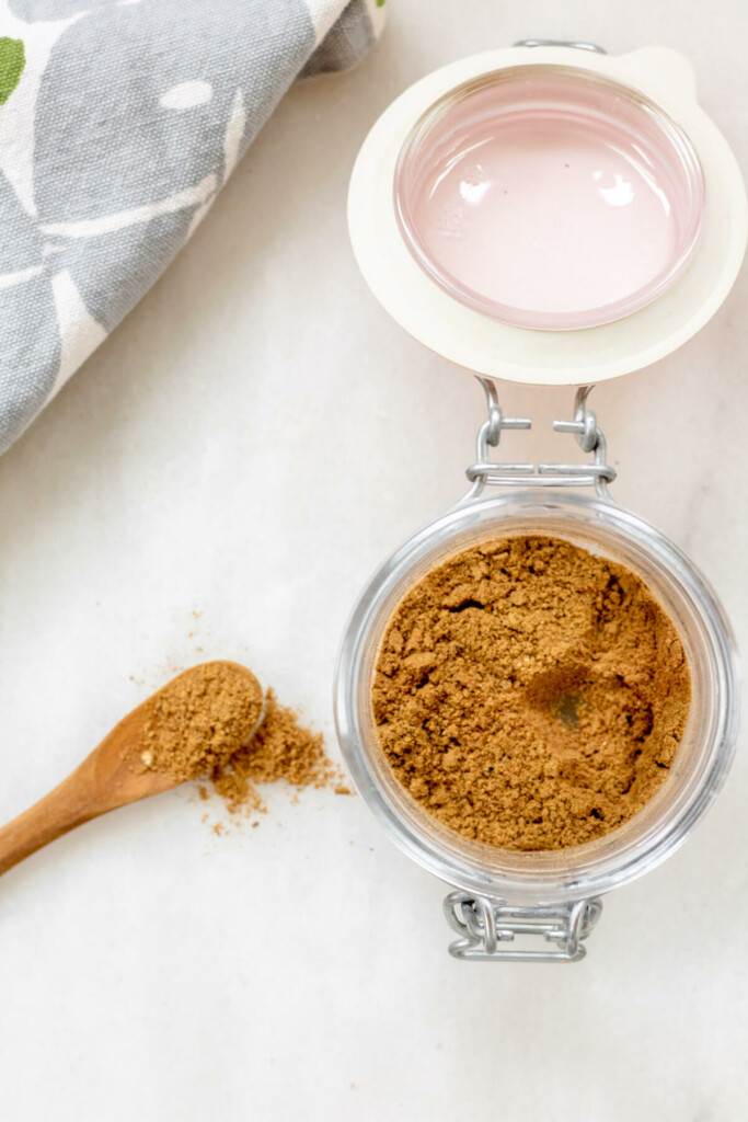 Small jar of a moroccan spice blend on a white background with an overflowing spoon on the side