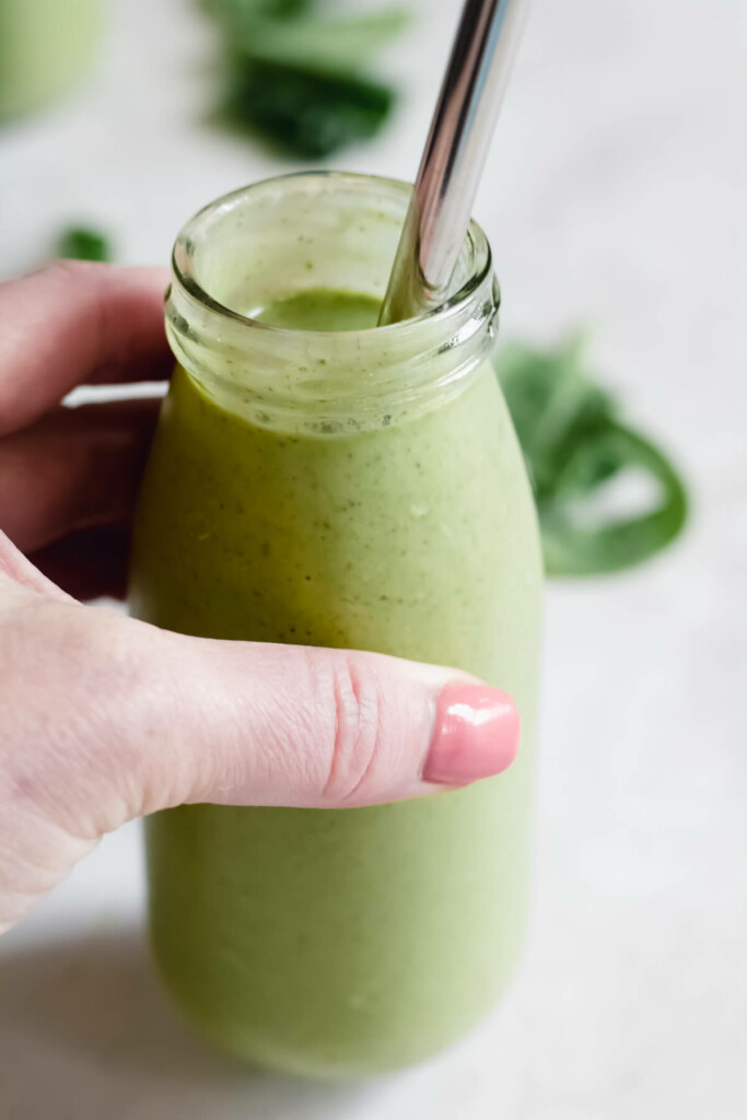 hand holding small jar filled with green smoothie