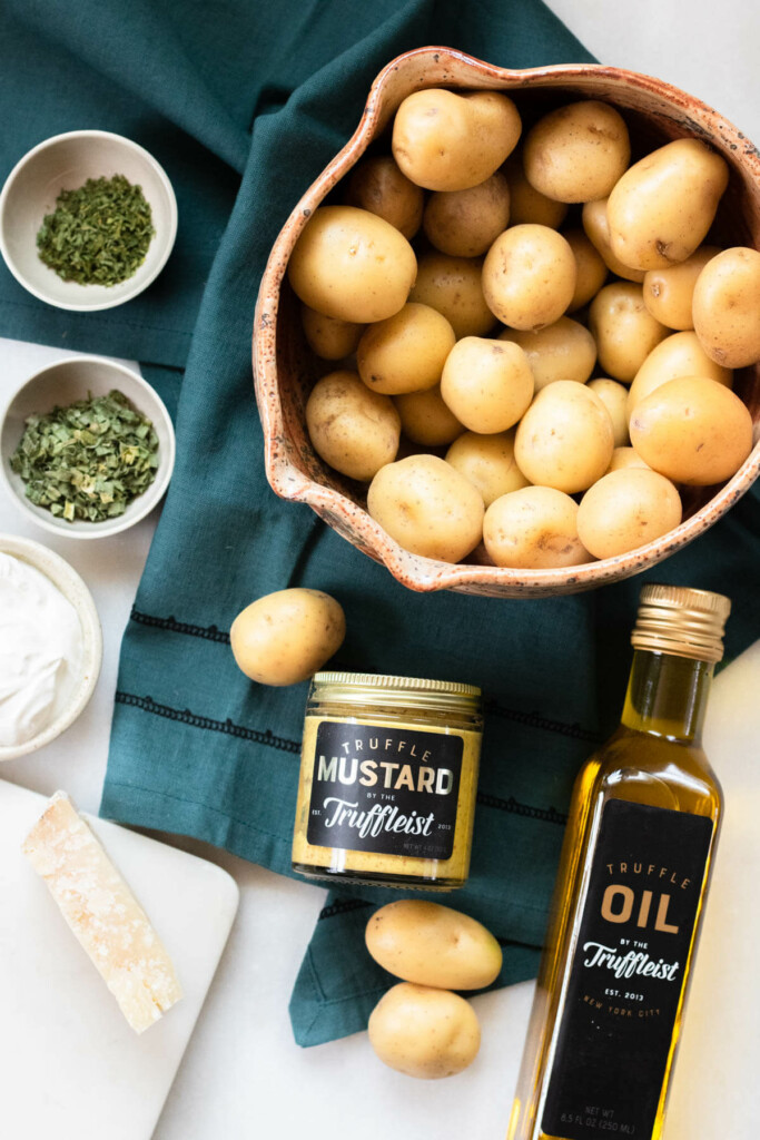 ingredients needed for truffle parmesan smashed potatoes, bowl of potatoes, truffle oil, parmesan cheese, chives, parsley, sour cream, and truffle oil
