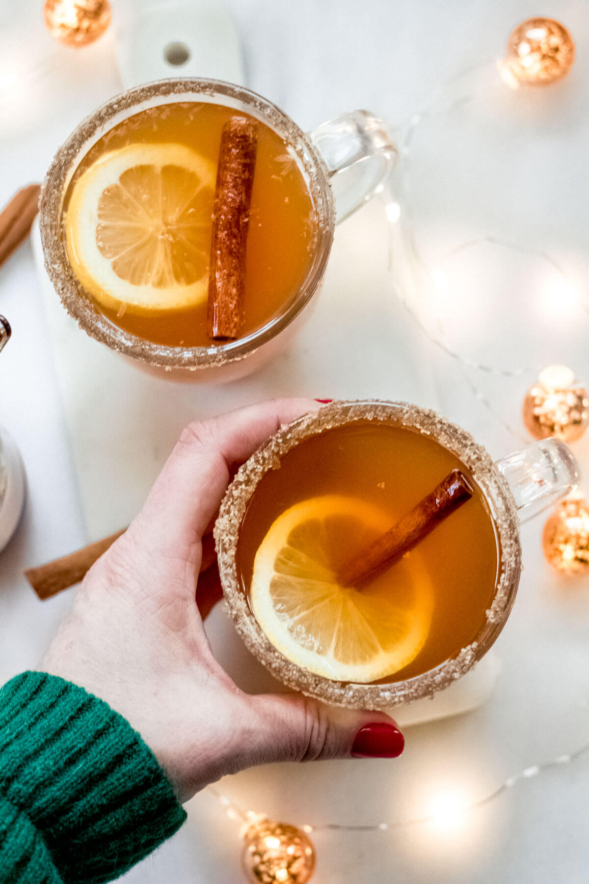 hand holding a peach cardamom hot toddy on a white background with twinkly lights