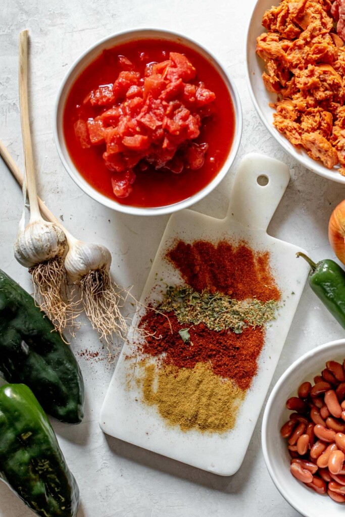 ingredients needed for chorizo poplano chili on. a white background, chorizo, poplano chilis, spices, tomato, and garlic