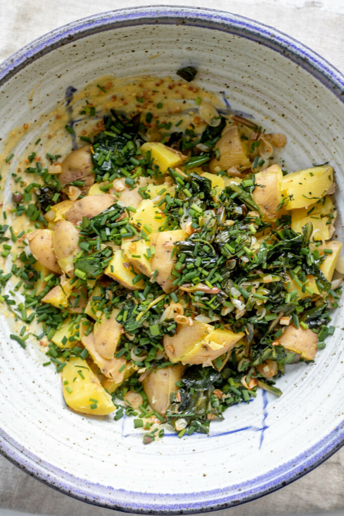 a bowl filled with cooked potatoes, cooked ramps, and herbs