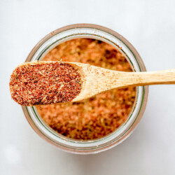 a wooden spoon overflowing with homemade cajun spice mix resting on a glass jar on a white background