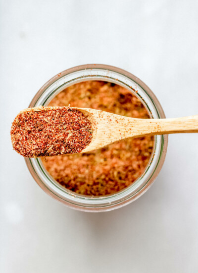 a wooden spoon overflowing with homemade cajun spice mix resting on a glass jar on a white background
