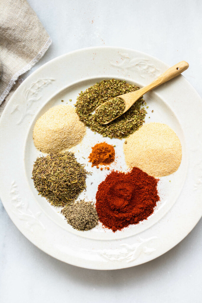 a white plate filled with several spices preparing to be mixed for homemade cajun seasoning