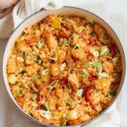 large white cast iron skillet with cajun shrimp and rice, two hands holding skillet