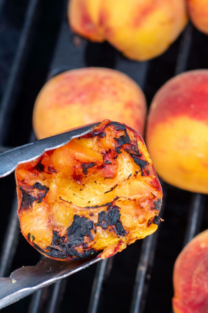 metal tongs holding a peach that has been grilled