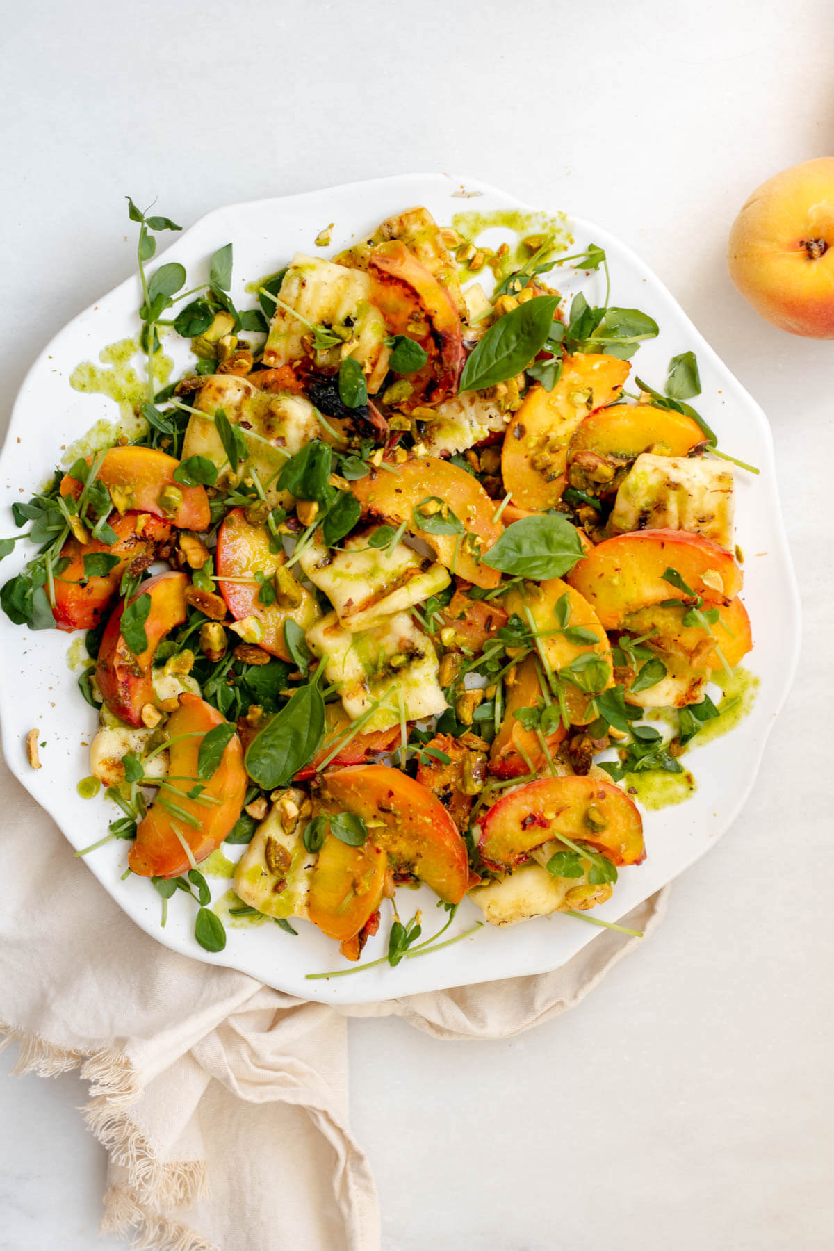 white plate filled with beautiful peaches, halloumi cheese, and pistachios