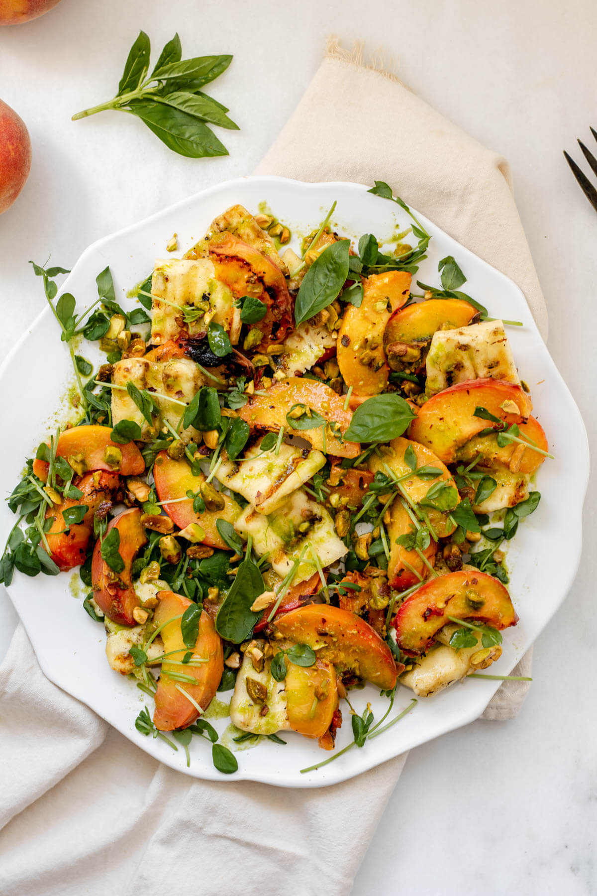 white plate filled with beautiful peaches, halloumi cheese, and pistachios