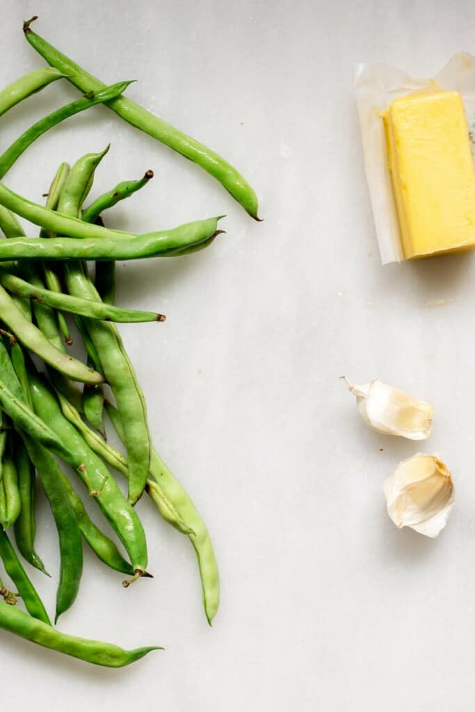 ingredients needed for air fryer green beans. green beans, butter, and garlic on a white background
