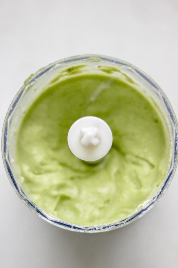 a small food processor with creamy avocado crema whipped up inside of it