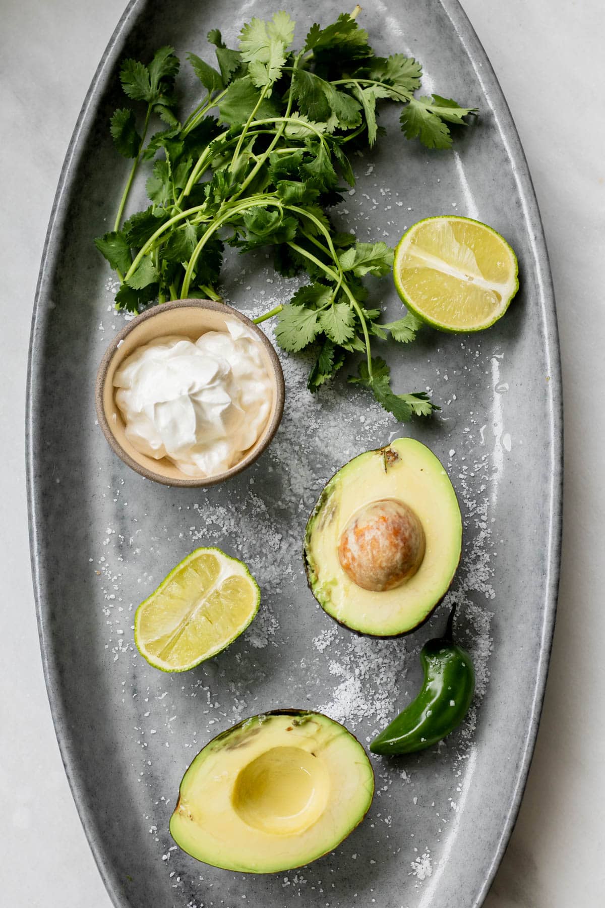 avocado, lime, jalapeno, sour cream, cilantro, and salt on a grey platter