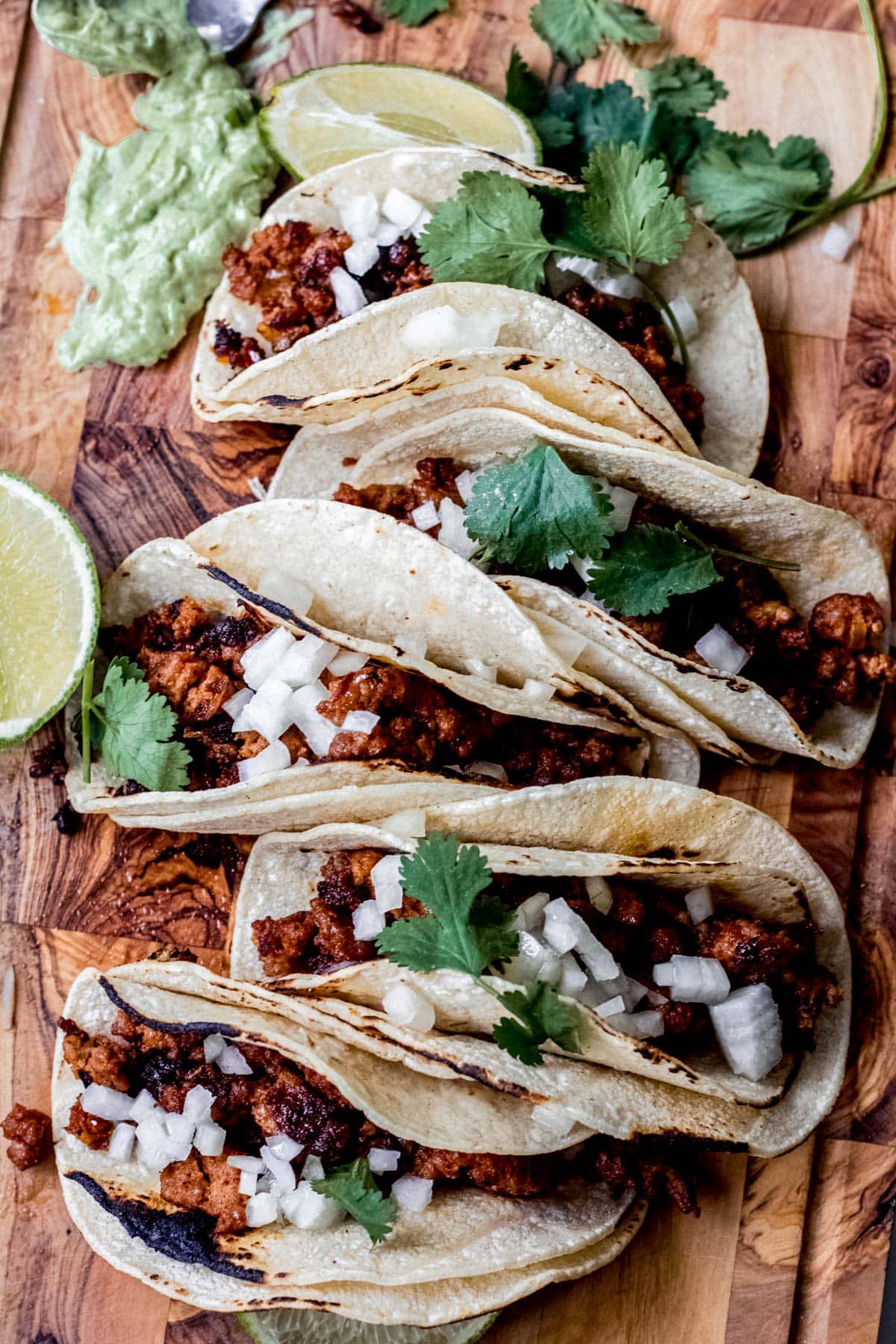 Chorizo tacos with diced onion, cilantro and avocado on a wooden cutting board