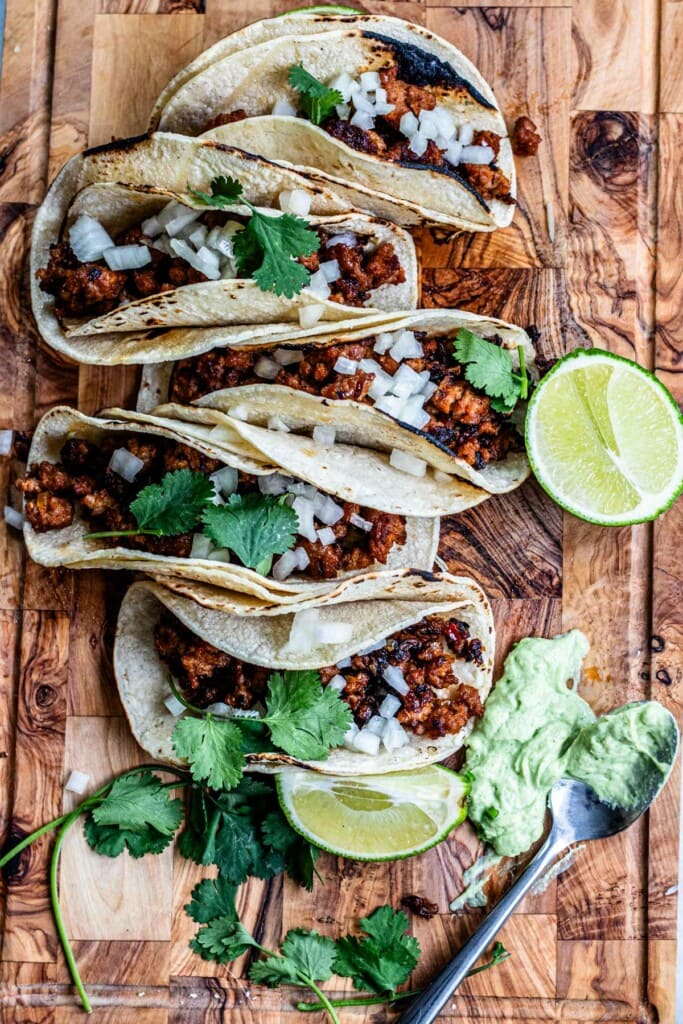 chorizo tacos on a cutting board with lime and cilantro and avocado crema on board