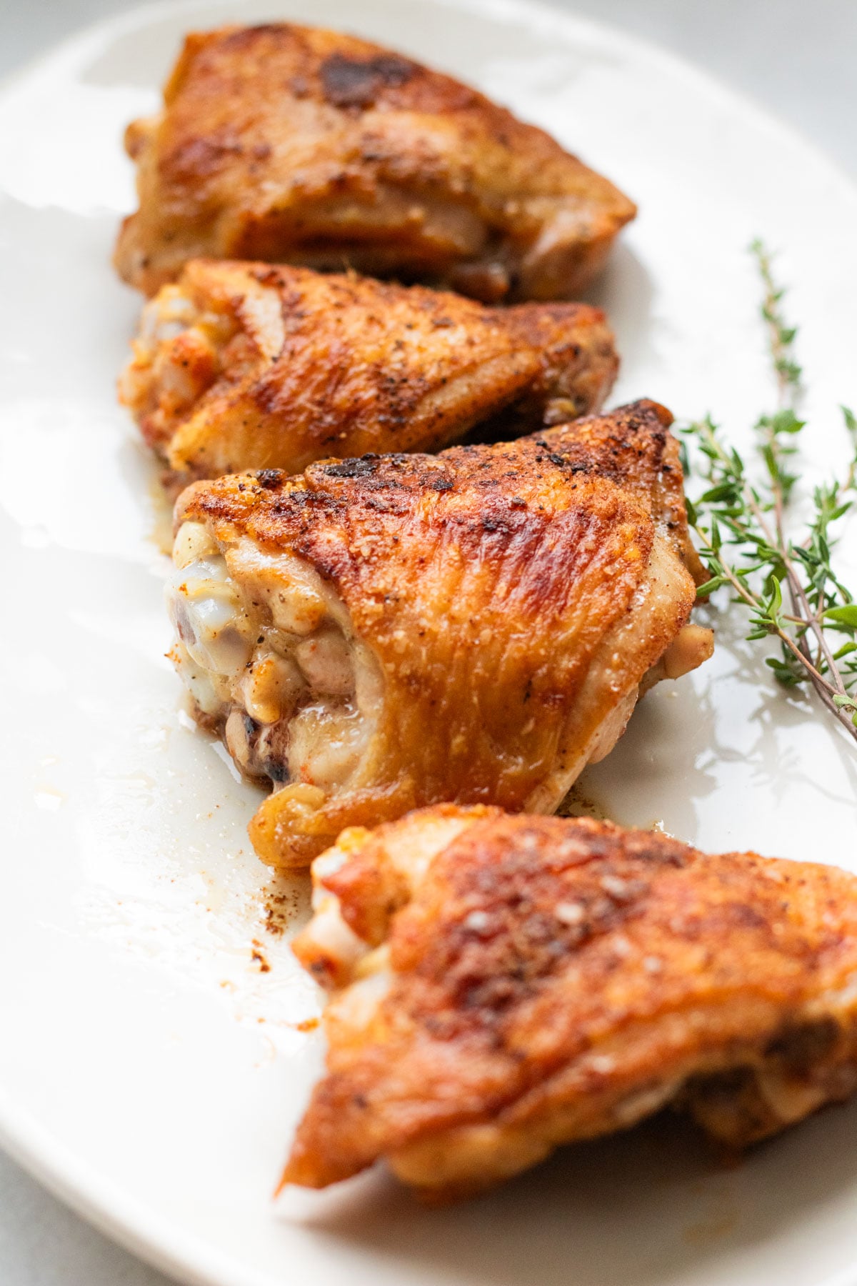 4 crispy chicken thighs on a white platter with fresh thyme