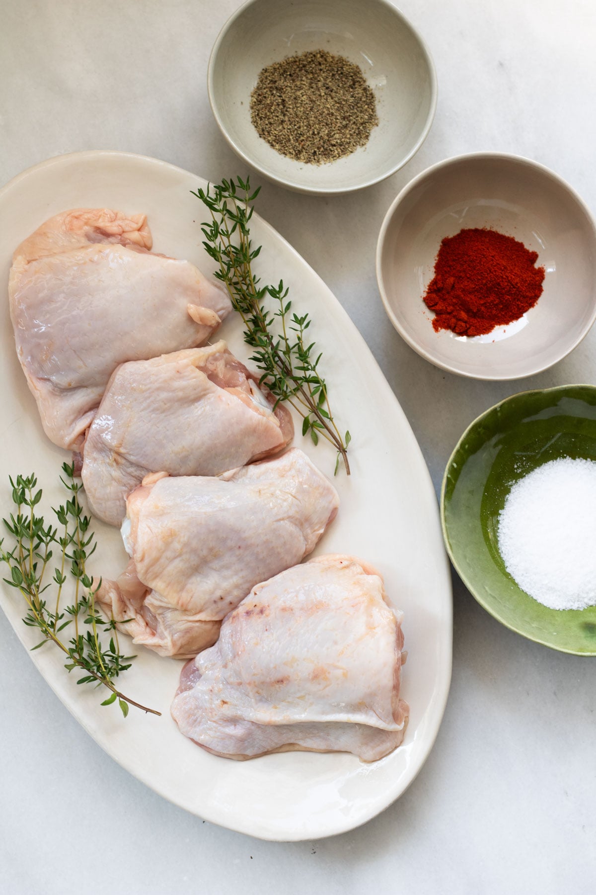 a plate of chicken thighs and bowls of seasoning, ingredients needed to make crispy chicken thighs