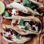 4 corn tortillas with chorizo, white onion and cilantro on a wood surface