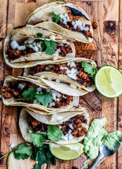 chorizo tacos on a cutting board with lime and cilantro and avocado crema on board
