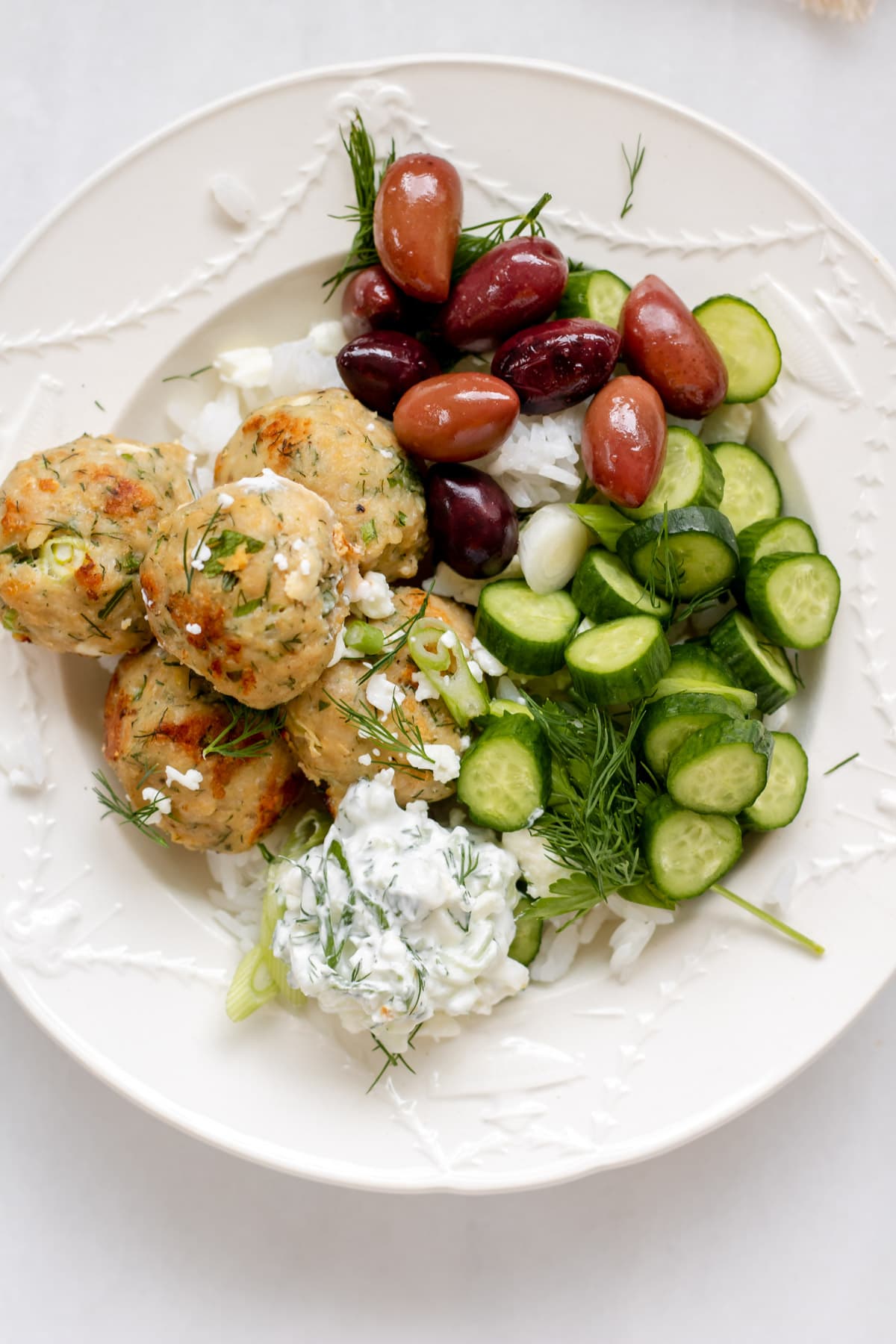 a bowl of greek meatballs with cucumbers and olives
