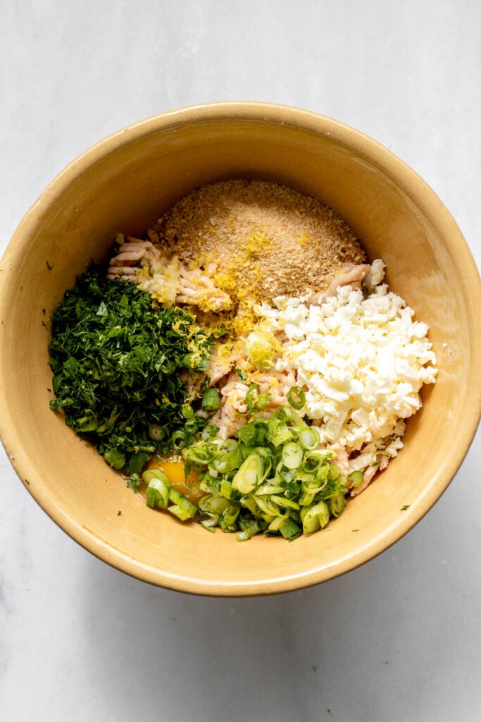 A bowl filled with chicken, herbs, and breadcrumbs for greek chicken meatballs