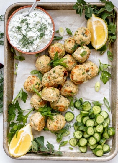 a tray full of greek chicken meatballs and cucumbers, dill, and yogurt sauce