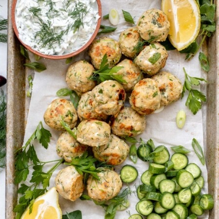 a tray full of greek chicken meatballs and cucumbers, dill, and yogurt sauce