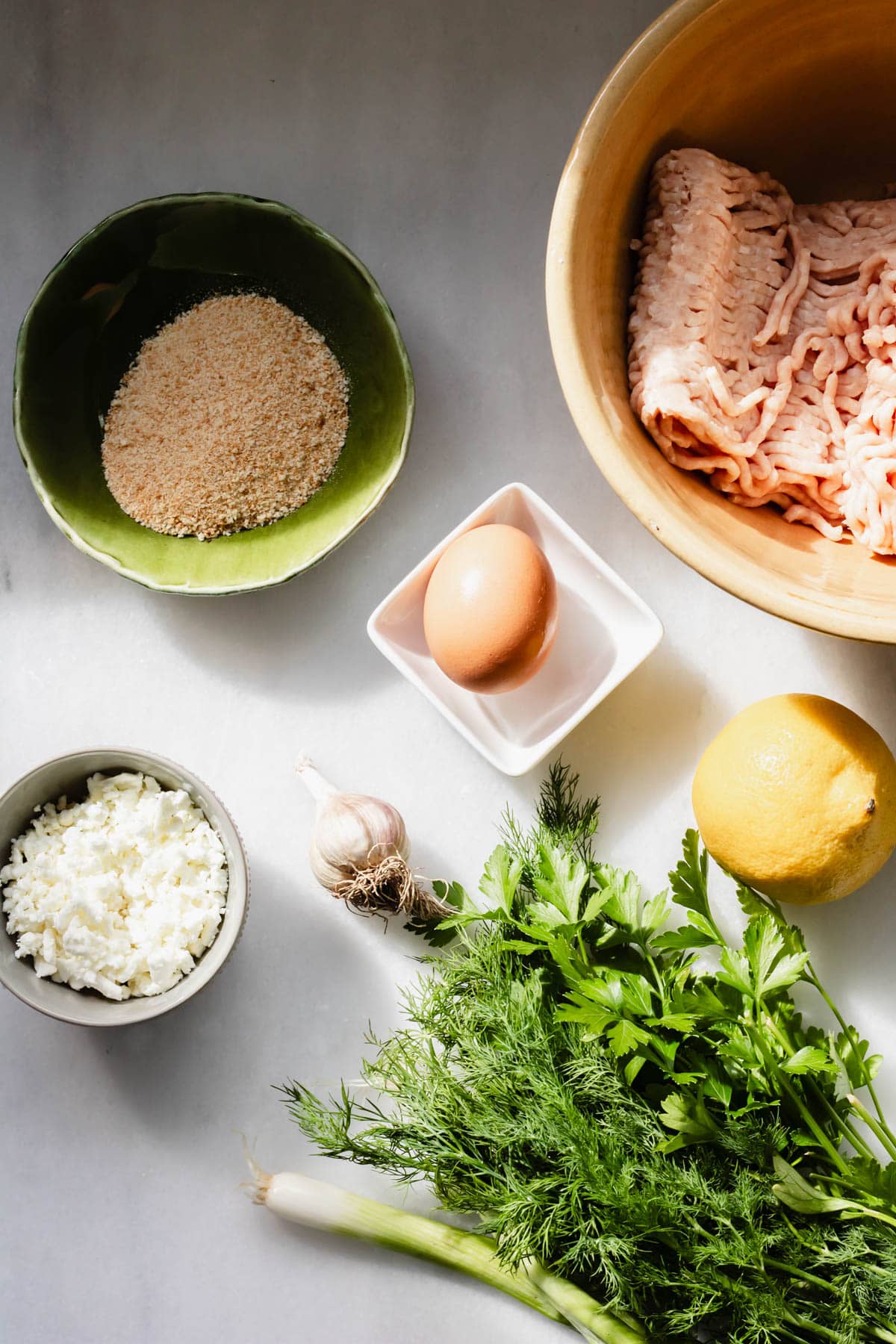multiple small and medium bowls filled with ingredients needed for greek chicken meatballs
