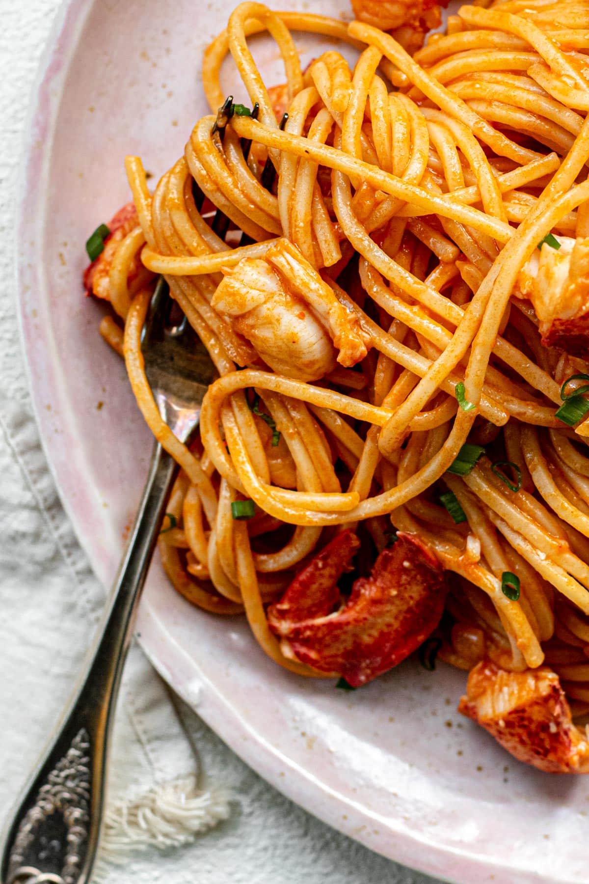 A plate of lobster pasta on a pink plate on a white background