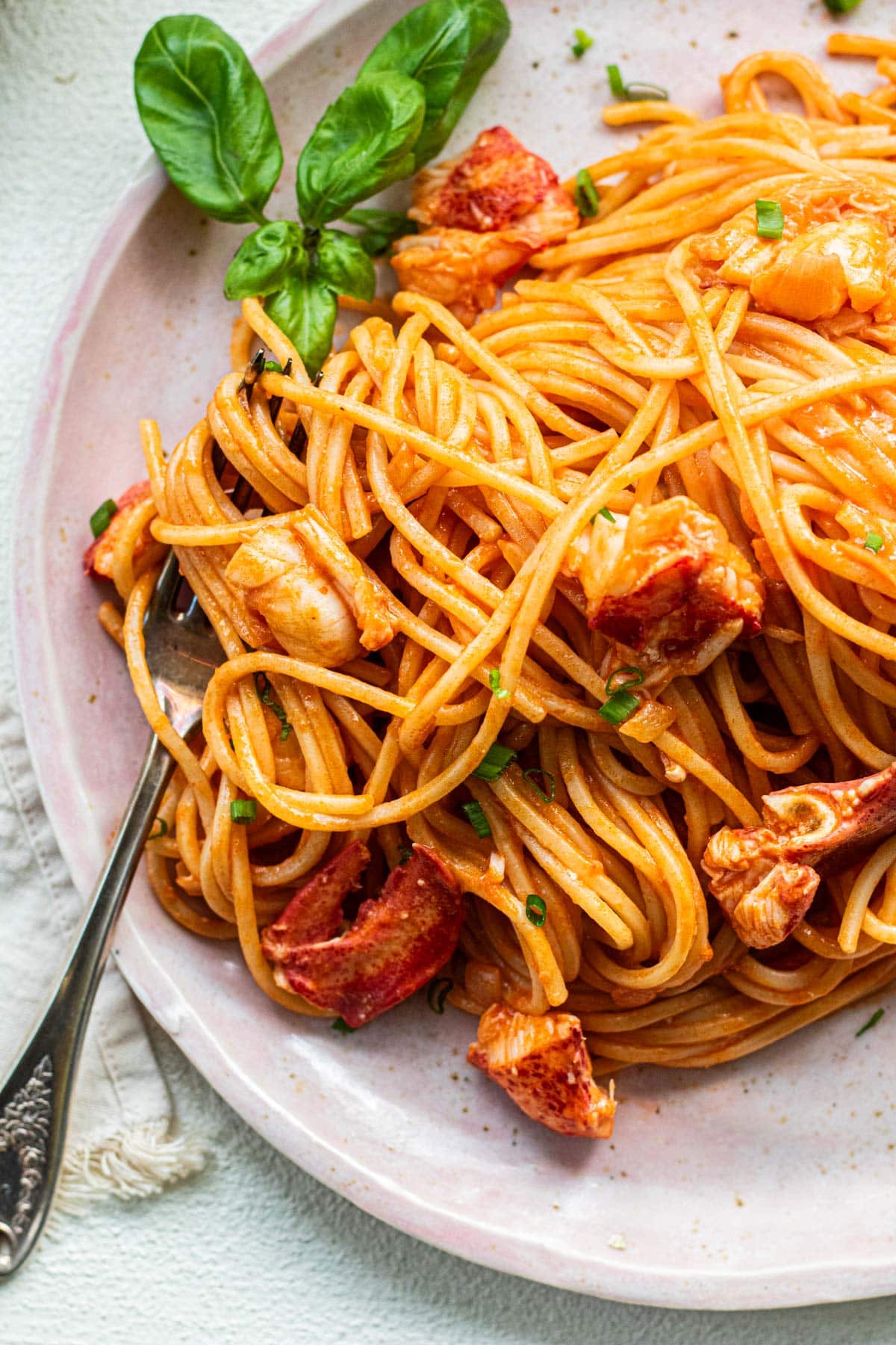 A plate of lobster pasta on a pink plate on a white background