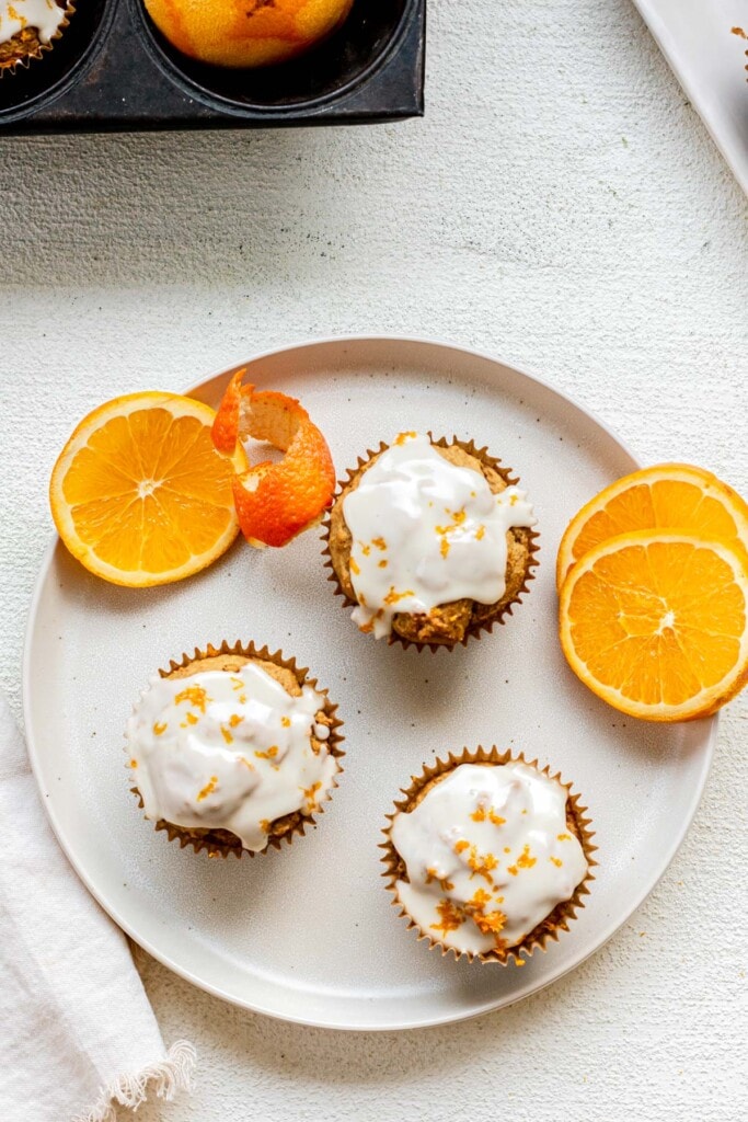 3 orange muffins on a white plate with orange glaze on top