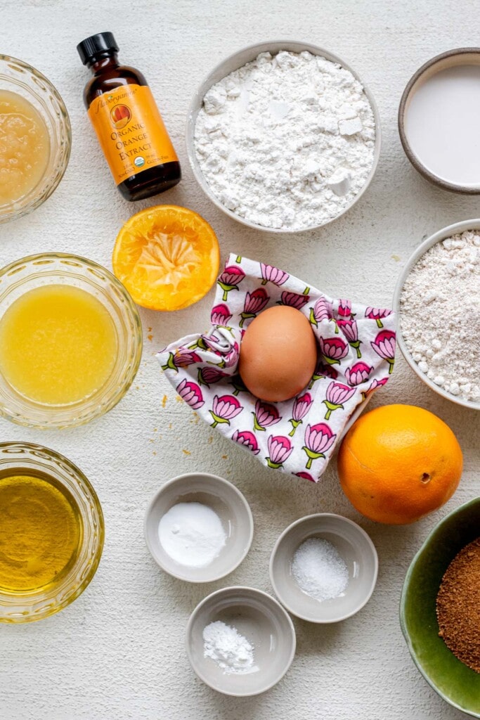 ingredient laid out on a white background for gluten free orange muffins including oat flour, eggs, applesauce, olive oil, and coconut sugar