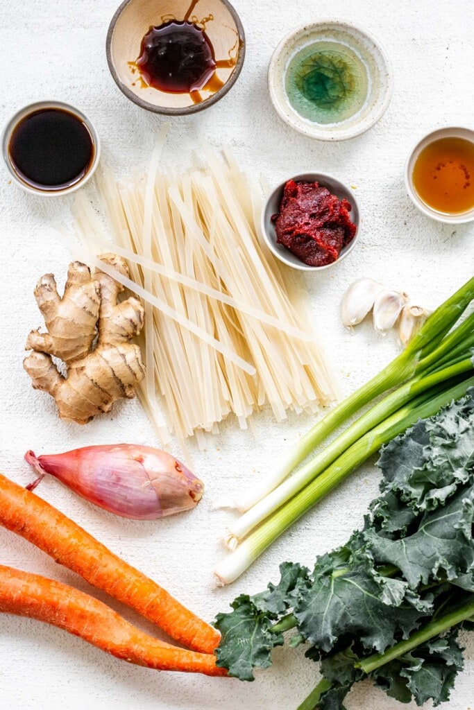 Ingredients on a white background including noodles, spices, kale, and carrots for spicy gochujang noodles