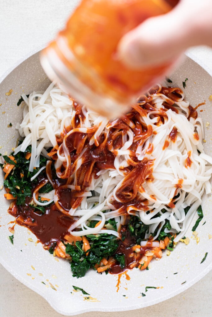 pouring gochujang sauce over noodles and vegetables