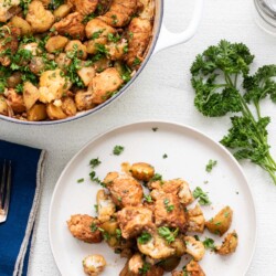 large white pot of chicken and potatoes with a white plate of chicken and potatoes with parsley